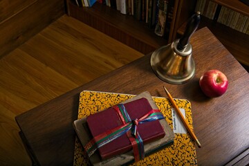 Overview of antique school desk concept with textbooks composition book apple and hand bell beside bookcases