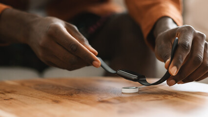 Young african american guy putting modern smartwatch for charging on wireless charger on wooden table, closeup