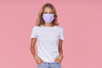 A young attractive woman in a white casual t-shirt wears a protective face mask. Protection against flu and cold diseases during a pandemic. Pink isolated background