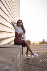 Pretty brunette woman in a leather skirt sitting in a sunset wearing sunglasses
