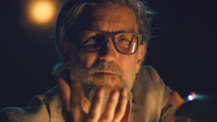 Serious director in glasses and casual suit at the table talking to the actors in the dim theater during the rehearsal of the play