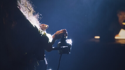 A woman with spinal muscular atrophy driving an electric wheelchair on a dim theater stage illuminated by a spotlight, during rehearsal with director