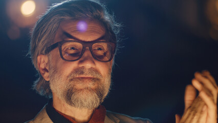 Happy director in glasses and suit smiling and applauding to actors after performance in the theater
