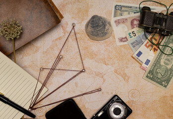 travel concept, you can see a beige background map with different objects such as a gun, old binoculars, notebook or diary made of recycled paper, pen, camera, money and lines representing the places 