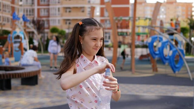 A preteen girl on the playground greedily drinks water from a plastic bottle. Active play on the playground.