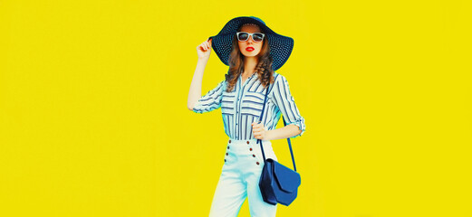 Portrait of beautiful woman model wearing black round straw summer hat, handbag and white striped shirt on yellow background