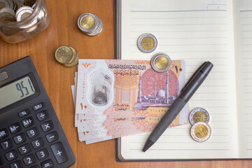 Egyptian Money, Plastic New Ten Egyptian Pound, Paper Banknotes and Coins on Wooden Desk, Calculator, Notebook and Pen, Closeup Top View, Space for Text - obrazy, fototapety, plakaty
