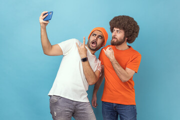 Portrait of funny cool two young adult hipster men blogger broadcasting livestream or taking...