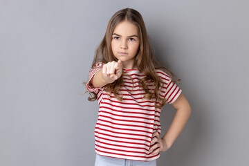 Portrait of strict dark haired little girl wearing striped T-shirt noticing and pointing finger to...