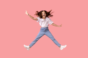 Fototapeta na wymiar Full length portrait of excited adorable little girl wearing white T-shirt jumping in air and spread arms, smiling happily, having fun. Indoor studio shot isolated on pink background.