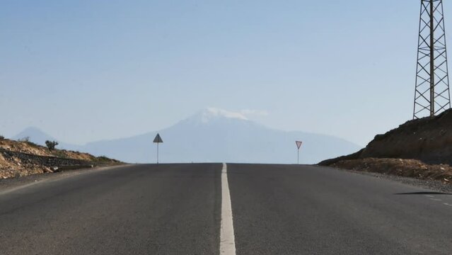 From a steep ascent along the highway, a view of a huge mountain with a gentle ridge on a hot summer day View of Ararat from the middle of the highway