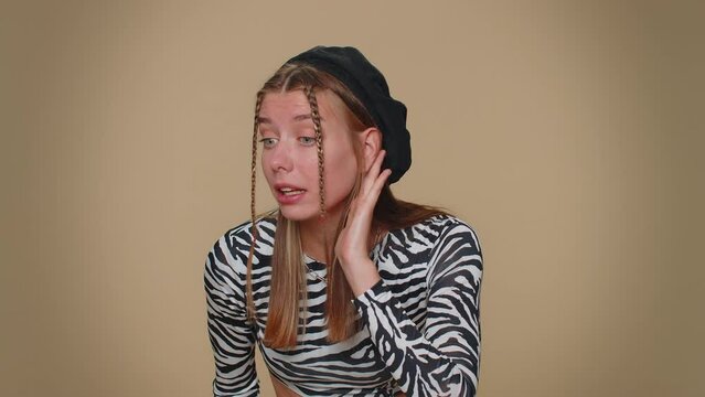 I cant hear you. What. Young woman trying hear you, looking confused and frowning, keeping arm near ear for louder voice, asking to repeat, to hear information, deafness. One girl on beige background