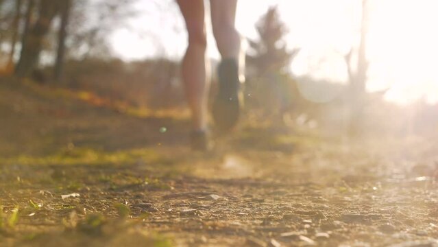 SLOW MOTION View of women's legs running away from the camera on dry gravel path. Female legs lifting dust while running away from the camera. Detailed view of sport activities in beautiful sunlight.