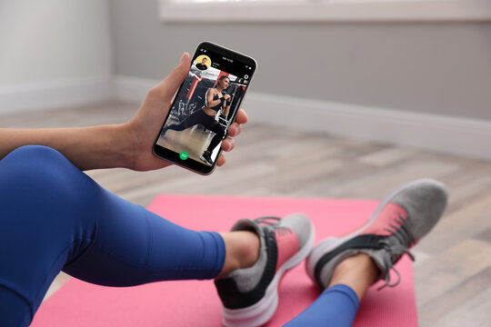 Woman having workout with personal trainer via smartphone at home, closeup