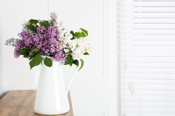 Beautiful lilac flowers in vase on wooden table near white wall. Space for text