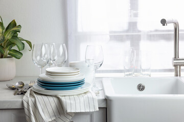 Fototapeta na wymiar Different clean dishware, cutlery and glasses on countertop near sink in kitchen, space for text