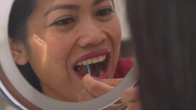 CLOSE UP: Mirror reflection of a woman flossing her teeth for tartar prevention. Beautiful young lady using dental floss toothpick for taking care of dental hygiene. Morning routine for a nice smile.