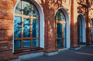 Entrance door made of glass and plastic in an old red brick building. Reflections and shadows of tree foliage on a summer morning. Blinds behind glass. Arched modern designs.