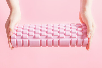 Female hands hold a massage foam roller on pink background close-up.