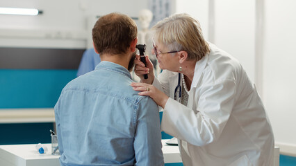 Female otolaryngologist consulting patient in medical cabinet, doing ear examination with otoscope....