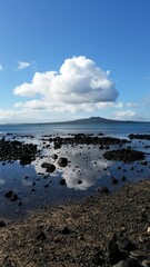 Large white fluffy cloud in a blue sky reflects in to the ocean sea with an island in the background on a sunny day