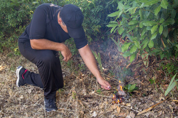 Image of a man dressed in black lighting a trigger to set fire to a forest. Reference to the problem of fires and arsonists