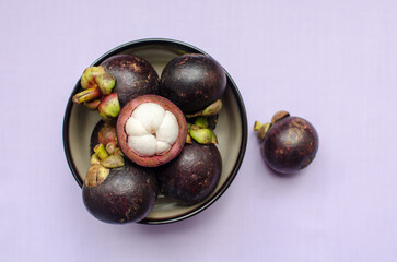 A vibrant bowl of mangosteens, exuding freshness and color, set against a serene light purple backdrop.
