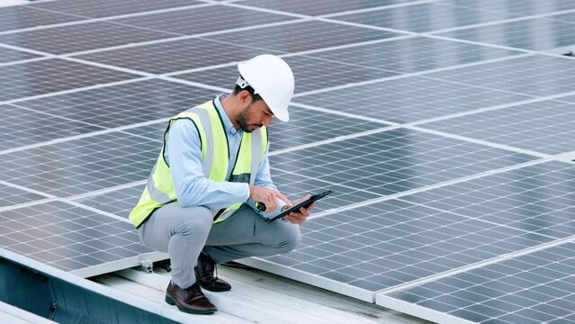 Young engineer or contractor inspecting solar panels on a roof in the city. One confident young manager or maintenance worker smiling while installing power generation equipment and holding a tablet