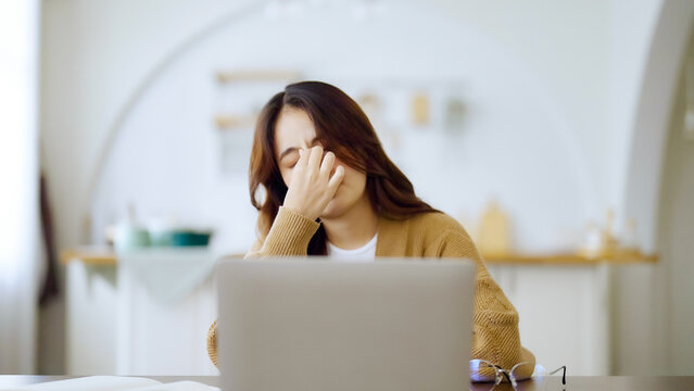 Overworked tired young asian woman feeling headache, having eyesight problem after computer laptop work. Stressed adult business woman suffering from fatigue rubbing dry eyes at home