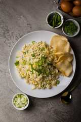 fried rice or nasi goreng kampung, with scrambled egg, spring onion and cracker on white plate