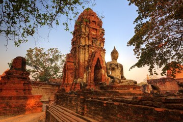 Morning scenery of Wat Mahathat, a ruined ancient Buddhist Temple, with a seated Buddha statue in meditation posture & ruins of majestic thai pagodas, in Ayutthaya Historical Park, Ayuthaya Thailand