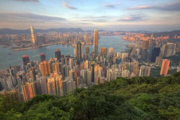 Sunset scenery of Hong Kong viewed from top of Victoria Peak, with city skyline of crowded skyscrapers by the harbour & Kowloon area across seaport ~ Beautiful cityscape of Hongkong in golden sunlight