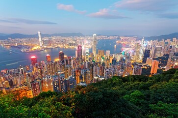 Beautiful city skyline of Hong Kong at night, viewed from top of Victoria Peak, with dazzling lights of crowded modern skyscrapers by Victoria Harbour & Kowloon area across seaport in blue twilight