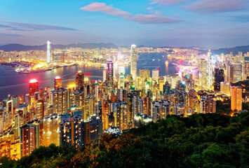 Fototapeta premium Beautiful city skyline of Hong Kong at night, viewed from top of Victoria Peak, with dazzling lights of crowded modern skyscrapers by Victoria Harbour & Kowloon area across seaport in blue twilight