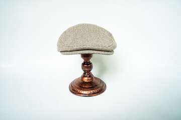 Detail of scally or flat cap in dark brown pattern  herringbone tweed fabric set on a bronze head mannequin on a white background