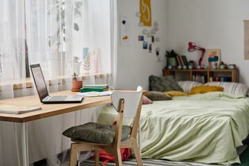 Horizontal image of modern teenage bedroom with comfortable bed and workplace with laptop
