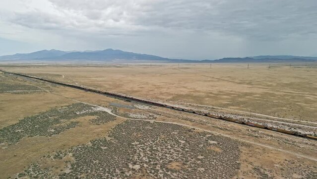 Aerial view of train tracks stretching through the Utah desert as cars sit on the tracks.