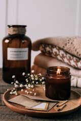 Burning candle in small amber glass jar, flowers of gypsophila and stack knitted seasin sweaters....