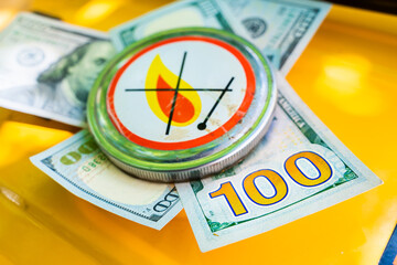 The number one hundred on a dollar bill with a gas tank cap pressed down with a flammability sign....
