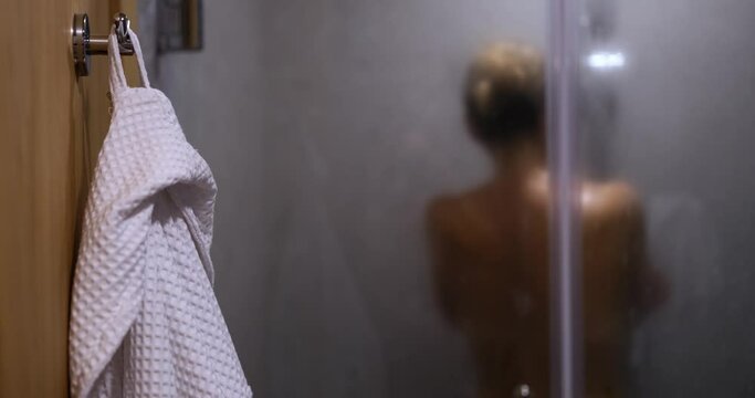White bathrobe hanging in bathroom against backdrop of woman washing herself 4k movie