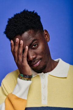 Portrait Of African Stylish Teenage Boy With Beads On His Arm Looking At Camera Against Blue Background