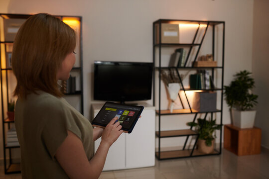 Woman dimming lights in apartment with help of smart home application on tablet computer