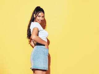 Young beautiful smiling female in trendy summer jeans skirt and top clothes. Carefree woman posing near yellow wall in studio. Sexy positive model having fun indoors. Cheerful and happy