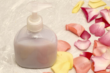 rose petals and a bottle of liquid soap on a gray textured background