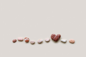 Creative arrangement of natural colored stones with heart. Smooth pebbles in row on beige background. Minimal trend summer flat lay, top view still life with sea pebble on the same line, copyspace