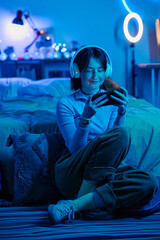 Teenage girl in wireless headphones sitting on floor playing video game in smartphone in dark bedroom © AnnaStills