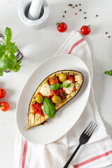 Grilled eggplant with mozzarella, cherry tomatoes, basil and olives on a plate on white background. Aubergine seasonal vegan recipe. Dieting, healthy nutrition. Restaurant menu. Top view