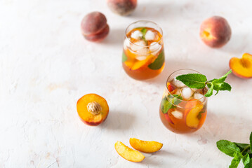Two glasses of sweet peach iced tea with mint on a white background. Fresh homemade summer lemonade with peaches. Dieting, healthy food, vegan. Copy space, product place.
