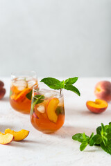 Refreshing iced tea with ripe peaches on a white background. Delicious peach iced tea Cuba Libre or Long Island iced tea cocktail in glasses. Summer cold fruit drink. Copy space