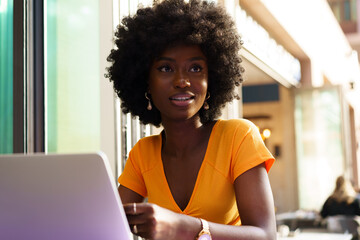 Happy beautiful young black woman using laptop in cafe